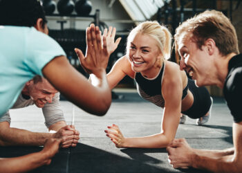 Two young women in sportswear high fiving together while planking on the floor during a gym workout class