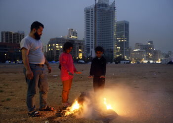 Przesiedleńcy wewnętrzni ogrzewają się przy ognisku w prowizorycznym obozie na nabrzeżu w Bejrucie. Fot. PAP/EPA/WAEL HAMZEH