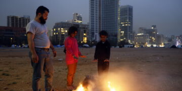 Przesiedleńcy wewnętrzni ogrzewają się przy ognisku w prowizorycznym obozie na nabrzeżu w Bejrucie. Fot. PAP/EPA/WAEL HAMZEH